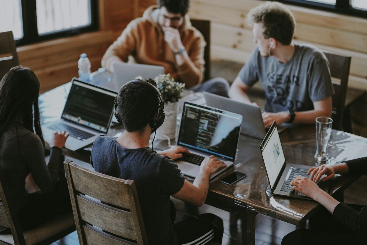 Cuatro personas trabajando en sus laptops alrededor de una mesa de madera
